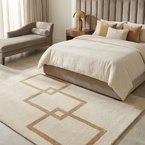 May include: A rectangular area rug featuring a cream-coloured base with a prominent geometric pattern outlined in tan jute-like material. The design consists of three interconnected rectangular shapes centred on the rug's surface.