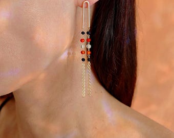 Può includere: Orecchini color oro con parte superiore a forma di U e catenine pendenti. Gli orecchini presentano una serie di perline colorate in nero, rosso e trasparente, aggiungendo un tocco di vivacità. Il design è elegante e adatto a varie occasioni.