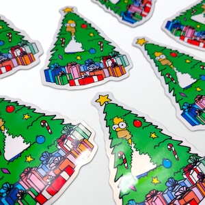 May include: A selection of stickers depicting a green Christmas tree design with Homer Simpson. The tree is adorned with baubles, candy canes, and a star. Colourful gift boxes are at the base of the tree.