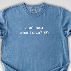May include: A blue t-shirt with the text "don't hear what I didn't say" in white. The shirt has a crew neck and short sleeves. The fabric appears soft and slightly wrinkled.