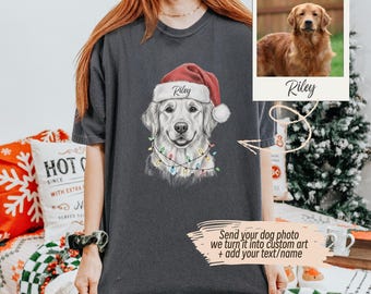 May include: Dark gray t-shirt featuring a Golden Retriever wearing a Santa hat with the name "Riley" and a string of Christmas lights. A photo of the dog is displayed next to the graphic. Text on the shirt says, "Send your dog photo we turn it into custom art + add your text/name."