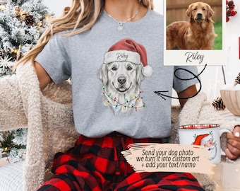 May include: A gray t-shirt featuring a custom illustration of a Golden Retriever wearing a Santa hat and Christmas lights. The dog's name, "Riley," is printed on the hat. A photo of the dog is also shown. Text on the image says, "Send your dog photo we turn it into custom art + add your text/name."