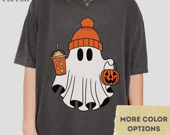 May include: Pepper-colored t-shirt featuring a cartoon ghost wearing an orange beanie and holding a pumpkin bucket and iced coffee. The shirt has the text "MORE COLOR OPTIONS" on a yellow banner.