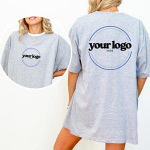 K&ouml;nnte beinhalten: Ein hellgraues T-Shirt mit kurzen &Auml;rmeln. Auf der Vorderseite des T-Shirts befindet sich ein kreisf&ouml;rmiges Logo-Design mit dem Text "your logo" in Schwarz. Auf der R&uuml;ckseite des T-Shirts befindet sich ebenfalls das gleiche Logo-Design. Das Shirt besteht aus einem weichen, bequemen Material.