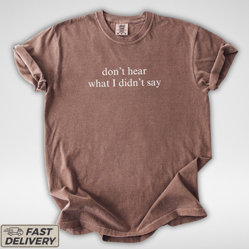 May include: A brown t-shirt with the phrase "don't hear what I didn't say" printed in white. The shirt has a crew neck and short sleeves. The fabric appears soft and slightly wrinkled.