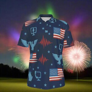 Puede incluir: Polo azul marino con un diseño patriótico con banderas americanas, águilas, estrellas y patrones de ondas rojas y blancas. La camisa tiene mangas cortas y cuello abotonado. El fondo muestra fuegos artificiales.
