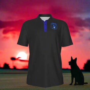 Puede incluir: Polo negro con cuello y botones azules, con un emblema azul en el pecho. La camisa est&aacute; colocada contra un fondo de puesta de sol con la silueta de un perro en primer plano.