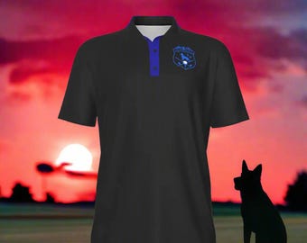 Peut inclure: Polo noir avec col et boutons bleus, orné d'un écusson bleu sur la poitrine. La chemise est placée devant un coucher de soleil avec la silhouette d'un chien au premier plan.