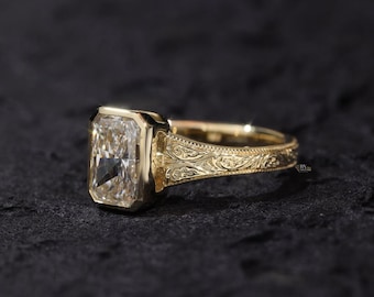 Könnte beinhalten: Ein goldener Ring mit einem großen, rechteckigen, klaren Edelstein. Der Ring hat ein verziertes, graviertes Design auf dem Band und um die Edelsteinfassung. Der Ring ist vor einem dunklen Hintergrund platziert.