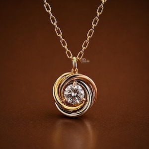 May include: A gold chain necklace featuring a circular pendant composed of three interlocking rings in yellow, rose, and white gold. A single round brilliant-cut diamond is set in the centre of the pendant. The text BN SOLITAIRE is visible.