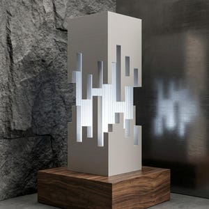 May include: A white rectangular lamp with a vertical cutout pattern revealing a ribbed translucent interior. The lamp is mounted on a square wooden base with a visible grain, emitting a soft light through the geometric openings.