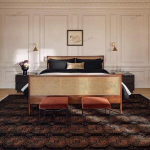 Pu&ograve; includere: Una camera da letto con un letto in legno con testiera intrecciata, biancheria da letto nera e due pouf color ruggine. Un tappeto fantasia e un'opera d'arte con un cigno incorniciato completano l'arredamento. La stanza ha una palette di colori neutri.