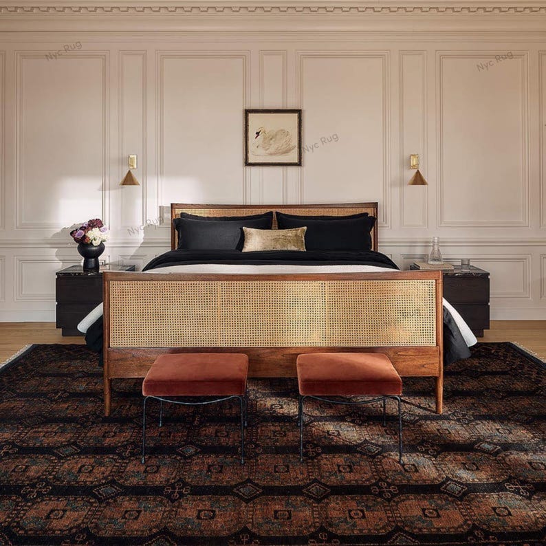 Pu&ograve; includere: Una camera da letto con un letto in legno con testiera intrecciata, biancheria da letto nera e due pouf color ruggine. Un tappeto fantasia e un'opera d'arte con un cigno incorniciato completano l'arredamento. La stanza ha una palette di colori neutri.