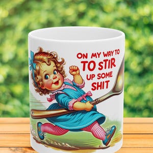 Może przedstawiać: Biały ceramiczny kubek z ilustracją w stylu vintage przedstawiającą dziecko z kręconymi włosami w niebieskiej sukience i różowych legginsach w paski, biegnące z dużą łyżką. Tekst głosi: ON MY WAY TO TO STIR UP SOME SHIT.