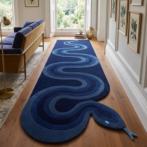 May include: A long, runner-style rug shaped like a snake, featuring a deep blue colour palette with lighter blue and navy concentric wave patterns. The rug has a distinct head section with a light blue eye detail and a protruding forked tongue.