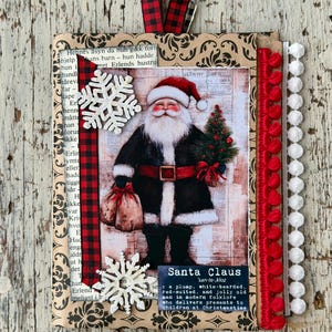 Può includere: Un biglietto decorativo con un'illustrazione di Babbo Natale in stile vintage, un nastro a quadri rossi e neri, fiocchi di neve bianchi glitterati, un bordo con pompon rossi e uno con pompon bianchi. Il testo definisce Babbo Natale.