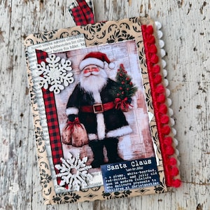 Può includere: Un biglietto decorativo rettangolare con un'illustrazione centrale di Babbo Natale in abito rosso e nero che tiene un piccolo albero e un sacco. Il biglietto è decorato con fiocchi di neve bianchi, nastro a quadri rosso e nero, pompon rossi e bianchi, con il testo 'Santa Claus'.