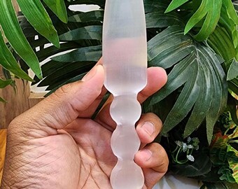 Könnte beinhalten: Ein klares, mattiertes Glasobjekt mit spitzer Spitze und einer Reihe von abgerundeten, bauchigen Formen entlang des Griffs. Das Objekt wird in einer Hand gehalten, mit einem Hintergrund aus grünem Laub.
