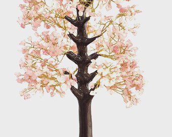 Pode incluir: Uma escultura decorativa de árvore com tronco e galhos marrons escuros, adornada com flores de cristal rosa. A árvore está em uma base redonda marrom escura coberta de pedras rosa e brancas. Os galhos têm arame dourado.