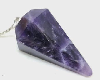 May include: A faceted, purple amethyst pendulum with a silver chain. The crystal is a deep violet color with lighter streaks and a pointed end. The pendulum is designed for divination and spiritual practices.