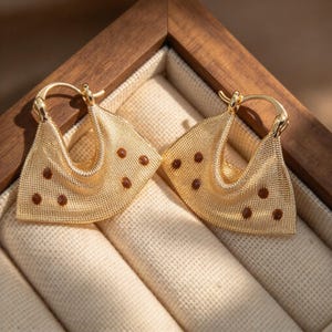 May include: A pair of gold-toned hoop earrings featuring a wide, fan-shaped design with a fine mesh texture. Each earring is accented with small, evenly spaced brown circular studs across the surface and includes a hinged closure mechanism.
