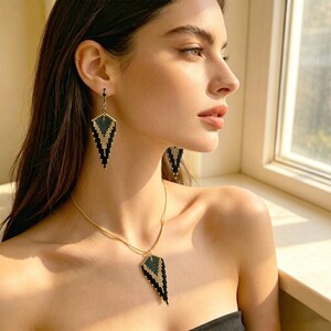 May include: A jewelry set consisting of a necklace and matching earrings, each featuring a triangular pendant crafted from small black, gold, and dark green beads. The necklace hangs on a thin gold chain, and the earrings are drop-style.