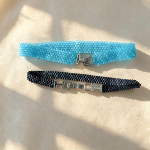 Può includere: Due braccialetti di perline, uno azzurro e uno nero, entrambi con una trama intrecciata. Il braccialetto azzurro ha una chiusura in metallo argentato, mentre quello nero presenta una chiusura in metallo argentato con piccole pietre incastonate.