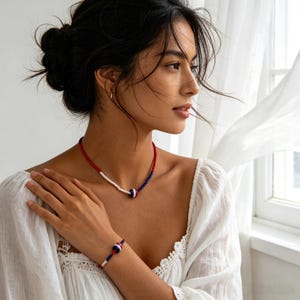 May include: A beaded necklace and matching bracelet set featuring small red, white, and blue beads. Both pieces include a single larger, spherical focal bead with horizontal red, white, and blue stripes centered on the strand.