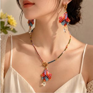 May include: A beaded necklace and matching drop earrings set featuring a multi-colored fish-shaped pendant and charms. The jewelry is crafted from small, vibrant glass beads in shades of red, orange, blue, and purple, finished with clear teardrop crystals.