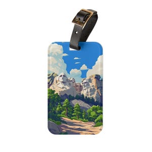 May include: A rectangular luggage tag with an illustration of Mount Rushmore under a blue sky with clouds. It has a black leather strap with a gold-coloured buckle. The tag's design includes green trees and a dirt path.