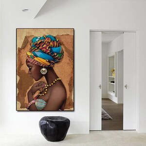 May include: A framed artwork shows a woman with dark skin wearing a vibrant head wrap, gold earrings, and a beaded necklace. The artwork has a brown, textured background. The woman is in profile, with her hand near her chest.