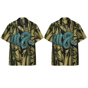 May include: A short-sleeved button-down shirt featuring a repeating pattern of a coiled teal snake set against a background of vertical yellow and black bamboo stalks. The shirt has a classic collar and a front button placket with white buttons.