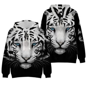 May include: A long-sleeved hooded sweatshirt featuring a high-definition graphic print of a white tiger face with piercing blue eyes. The design covers the front and back, showcasing black stripes against a white fur background and a black base.