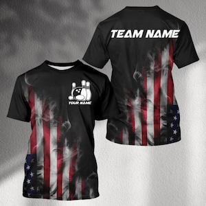May include: Black bowling t-shirt with an American flag design. The front features a bowling pin and ball graphic with the text "YOUR NAME". The back of the shirt has the text "TEAM NAME" in white.
