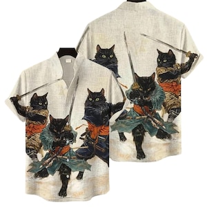 May include: A short-sleeved button-down shirt featuring a repeating pattern of black cats dressed as samurai warriors. The cats are depicted with swords and traditional Japanese attire in shades of black, green, orange, and tan on a light beige background.