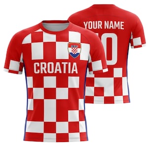 Puede incluir: Una camiseta de f&uacute;tbol de Croacia a cuadros rojos y blancos con la palabra "CROATIA" en el pecho y el escudo de armas croata. La parte trasera de la camiseta es roja con el texto "YOUR NAME" y el n&uacute;mero "0".