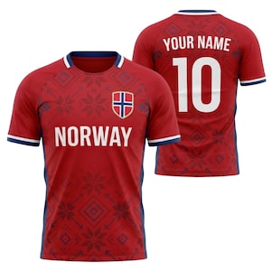 Op de afbeelding: Rood Noorwegen voetbalshirt met de witte tekst "NORWAY" op de voorkant en het nummer "10" op de achterkant. Het shirt heeft een Noors vlaglogo en een sneeuwvlokpatroon. De mouwen en kraag hebben blauwe en witte afwerking.