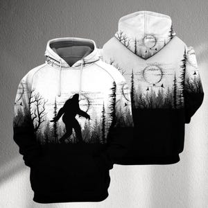 May include: Black and white hooded sweatshirt with a Bigfoot silhouette in a forest scene. The design includes a full moon, trees, and birds. The back of the hoodie also features the forest and moon design.