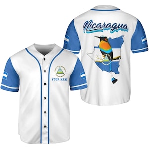 May include: White baseball jersey with blue sleeves and trim. The front features a crest and the text "YOUR NAME". The back displays "Nicaragua" above a map outline with a colorful bird and flag.