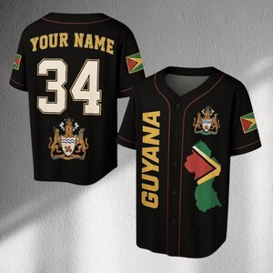 May include: Black baseball jersey with the word "GUYANA" in gold lettering on the front. The jersey features the Guyana coat of arms, flag, and a map outline. The back has the number 34 and the text "YOUR NAME" in gold.