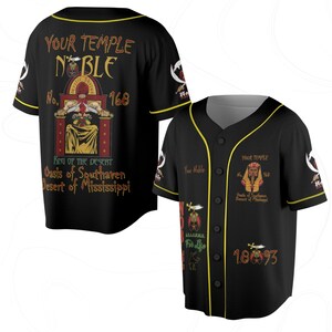 May include: Black baseball jersey with yellow trim and button closure. The jersey features the text "YOUR TEMPLE NOBLE" and "168" on the front and back, along with graphics and text including "KING OF THE DESERT" and "Oasis of Southaven Desert of Mississippi".