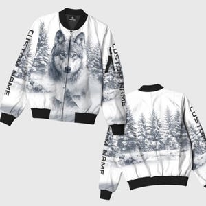 Peut inclure: Veste de bombardier blanche avec une illustration de loup et une scène de forêt enneigée. La veste a des bordures noires sur le col, les poignets et l'ourlet, avec les mots "CUSTOM NAME" imprimés sur les manches.