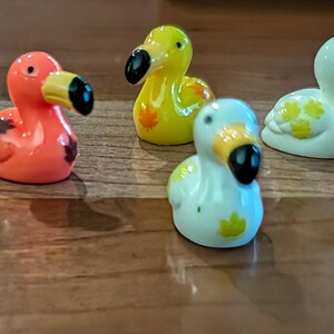 May include: A collection of small, colorful dodo bird figurines. The figurines are in various colors, including yellow, orange, white, and blue, with black beaks and eyes. Some have decorative markings.