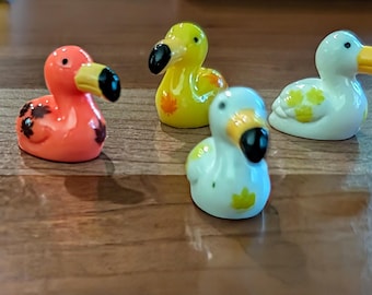 May include: A collection of small, colorful dodo bird figurines. The figurines are in various colors, including yellow, orange, white, and blue, with black beaks and eyes. Some have decorative markings.