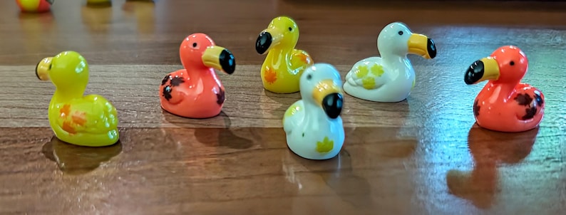 May include: A collection of small, colorful dodo bird figurines. The figurines are in various colors, including yellow, orange, white, and blue, with black beaks and eyes. Some have decorative markings.