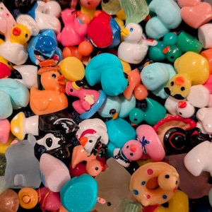 May include: A collection of colorful, small plastic figurines in various shapes, including ducks, mushrooms, and hearts. The figurines are in shades of pink, yellow, blue, and green, creating a playful and vibrant assortment. Some figurines have painted details.