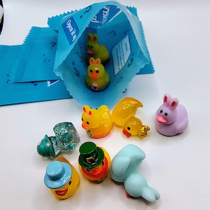 May include: A collection of colorful miniature figurines, including yellow ducks, a purple bunny, and a green-topped mushroom. Some figurines are inside a blue bag with the text "Open it up".