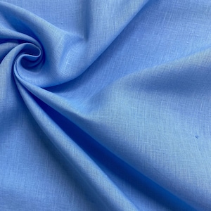 May include: Close-up of a light blue linen fabric. The fabric is folded and draped, creating shadows and highlights that emphasize its texture. The color is a soft, solid blue, suitable for clothing or home decor.