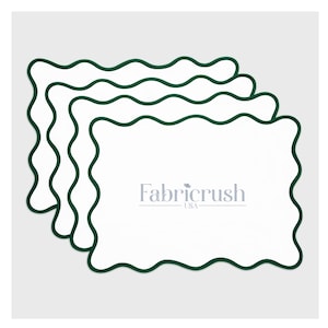Op de afbeelding: Vier witte rechthoekige placemats met een donkergroene golvende rand. De placemats zijn iets op elkaar gestapeld, waardoor het Fabricrush USA-logo in het midden onderaan zichtbaar is. Op een lichtgrijze achtergrond.