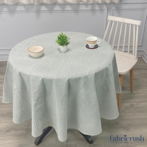 Puede incluir: Una mesa redonda con un mantel a rayas blancas y negras. Una pequeña planta en maceta, un cuenco y una taza de té con un platillo están sobre la mesa. Una silla blanca está al lado de la mesa. La mesa tiene unos 91 cm de diámetro.